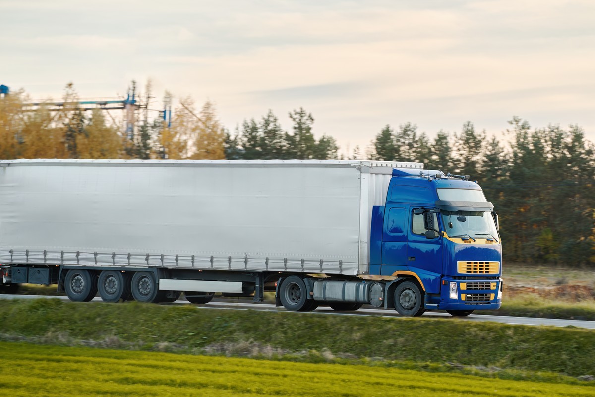 Commercial vehicles for shipping and post delivery drive on a motorway. White trucks with semi trailers carrying cargo containers. Sustainable and efficient logistics practices to transport goods.